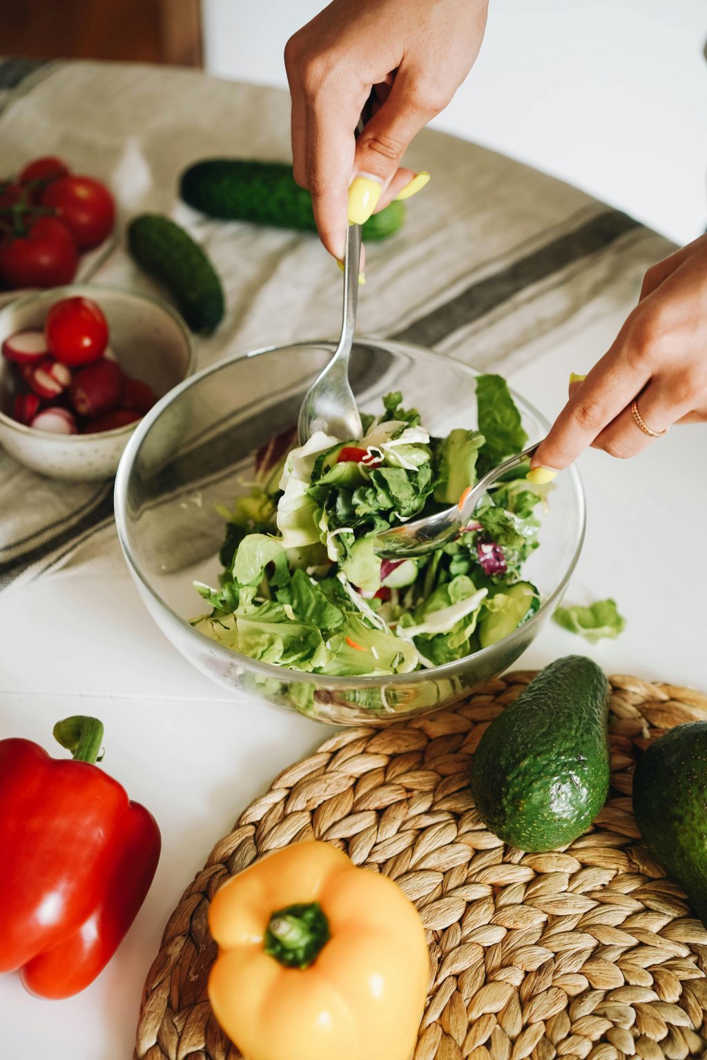 hands mixing a salad in a glass bowl with three different coloured capsicums on the bench
