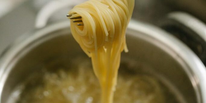 A pot of boiling water with sphaghetti in it. A female hand holds a fork with spaghetti wrapped around it over the pot