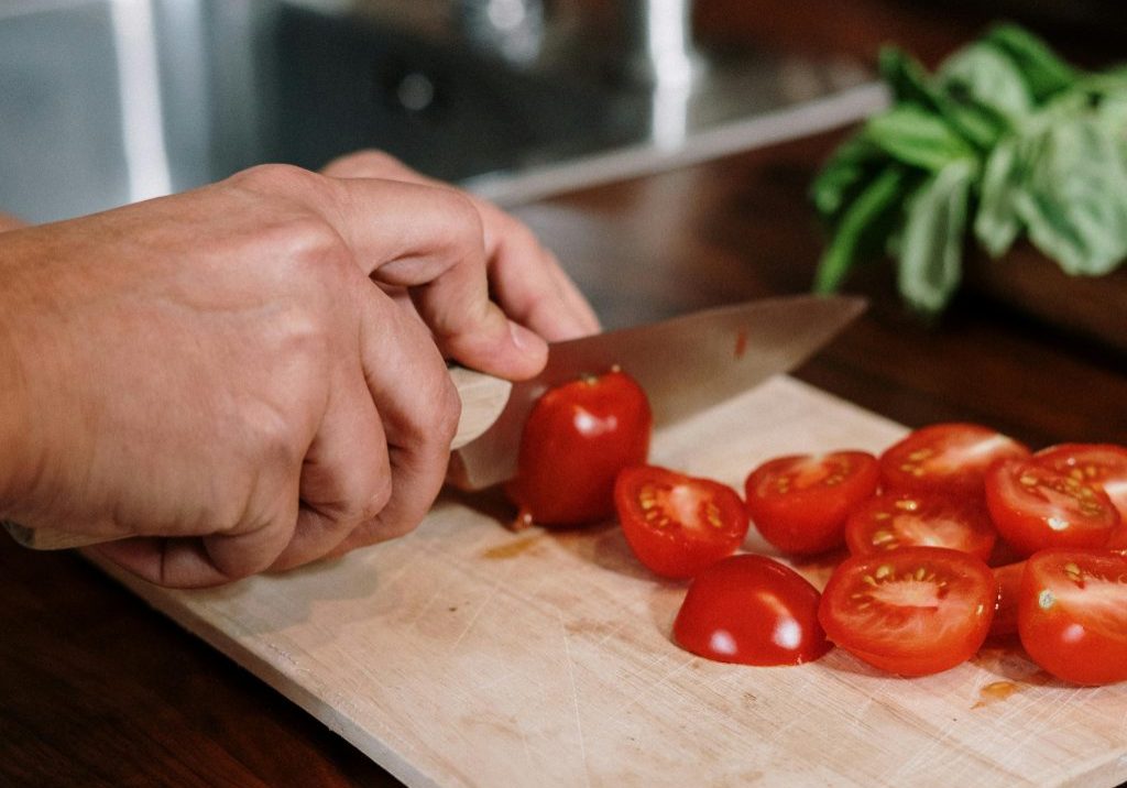hands chopping red toamtoes on a wooden chopping board