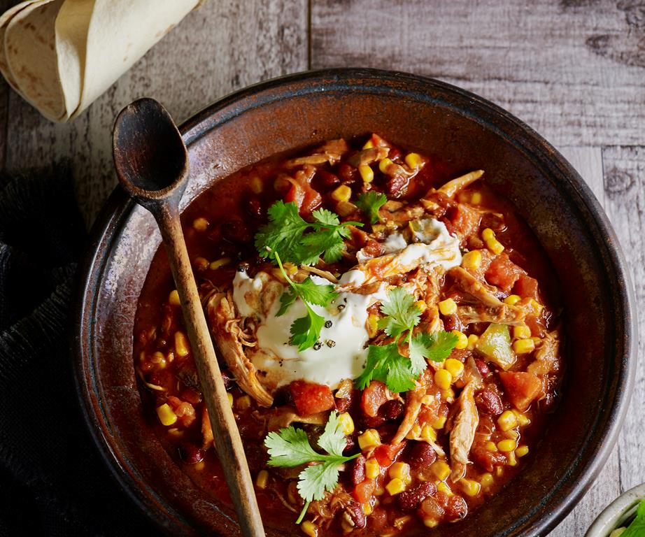 A bowl of shredded chicken cooked with beans and corn, topped with sour cream and coriander in a mexican sauce