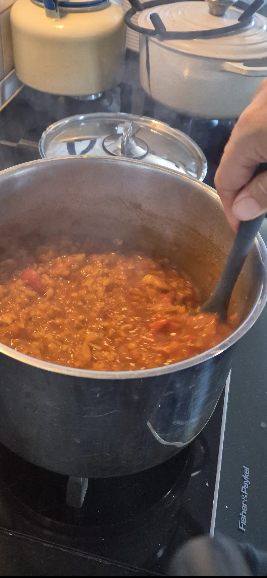 A pot of lentil soup simmering on a stove with a female hand stirring it in a pot