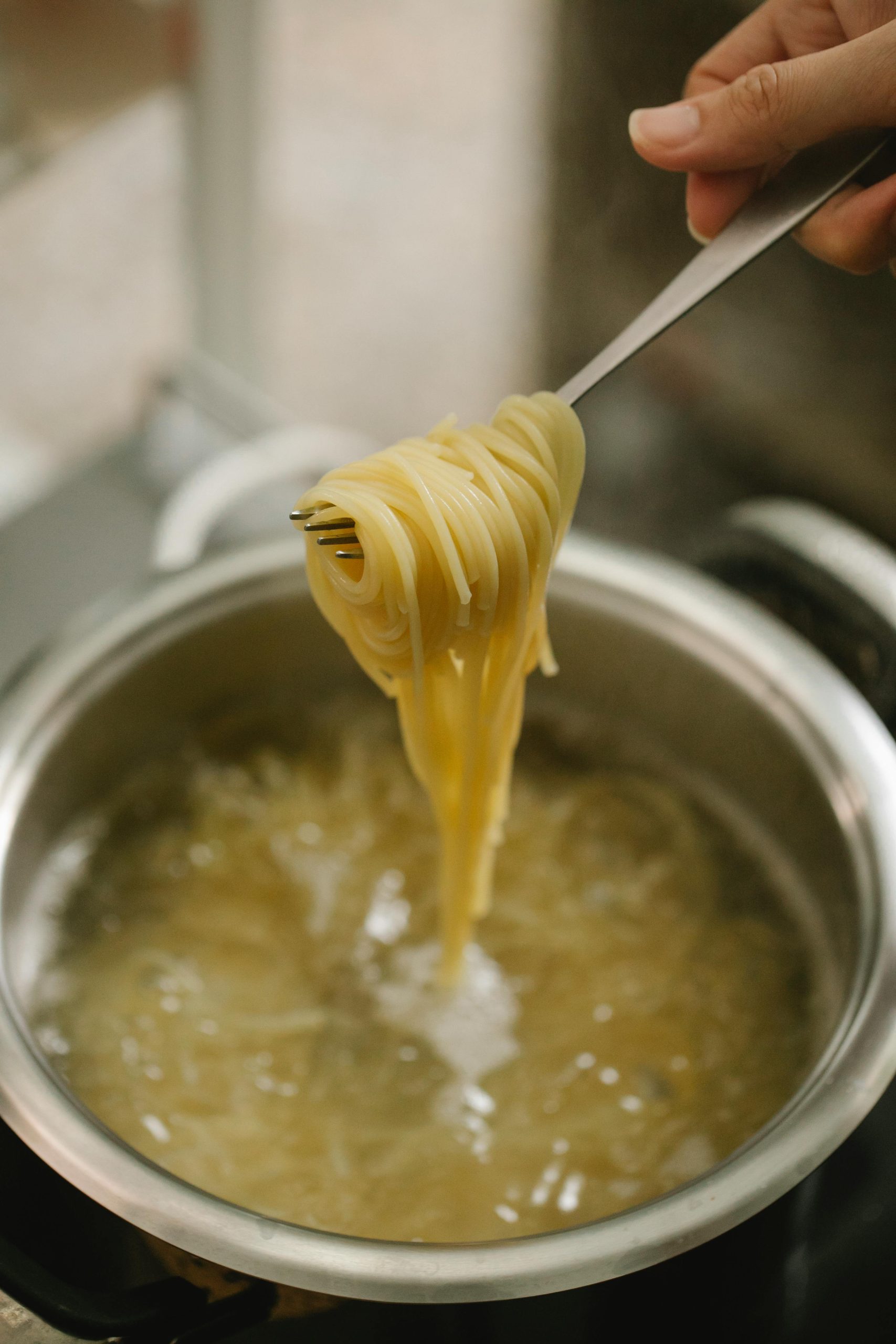 A pot of boiling water with sphaghetti in it. A female hand holds a fork with spaghetti wrapped around it over the pot