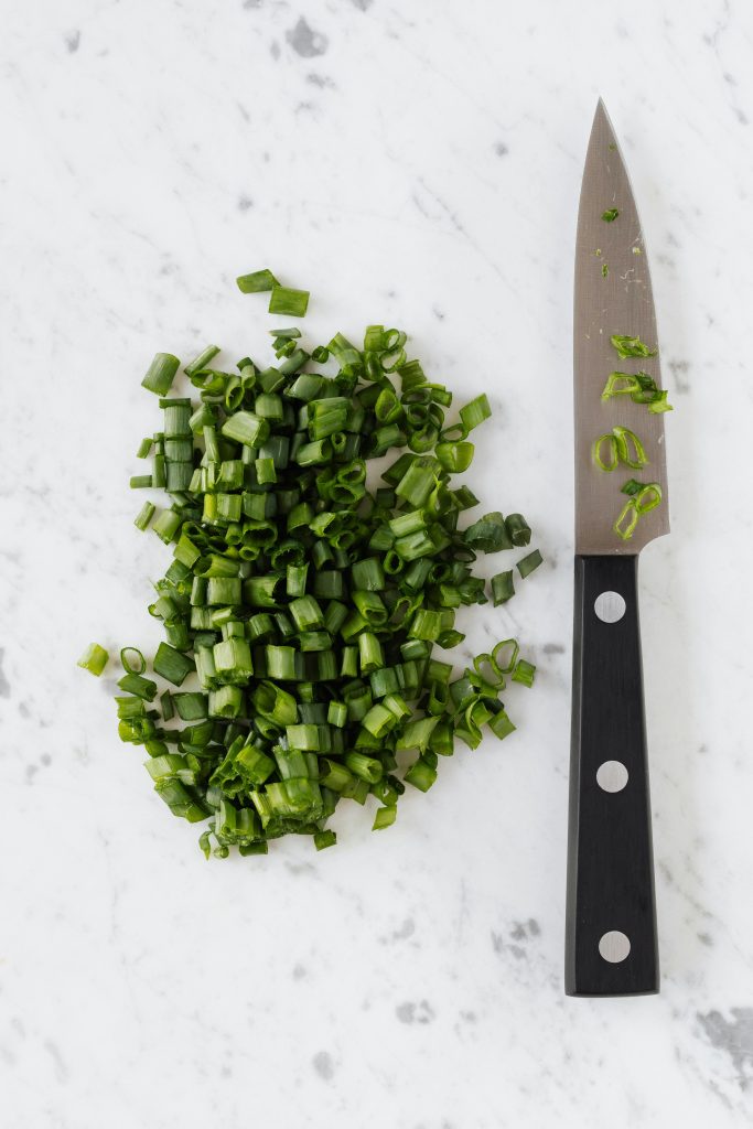 A black knife is sitting next to green chopped herbs on a marble board